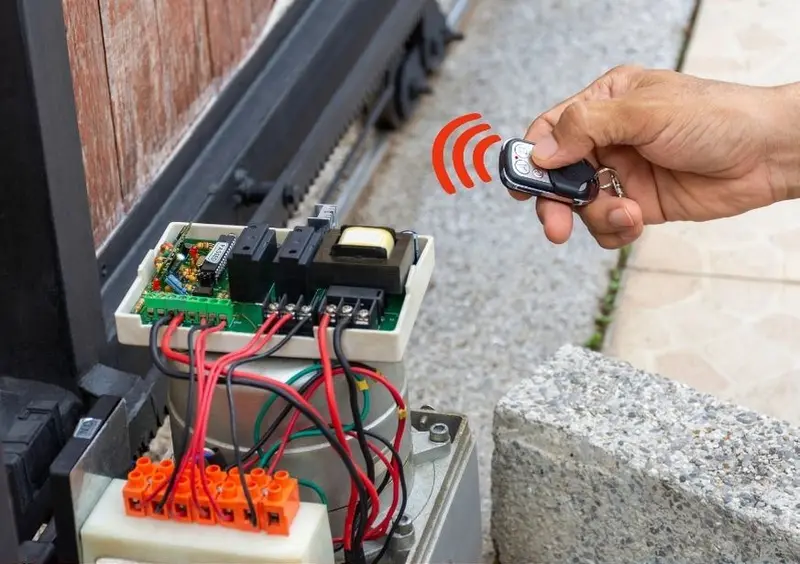 Open sliding gate motor control box next to a hand holding a gate remote