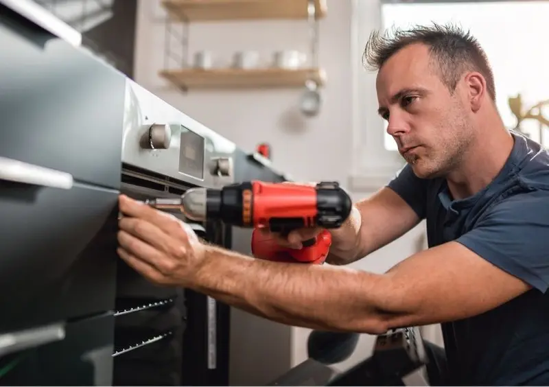 Man using a cordless drill to fit a built-in oven in a kitchen