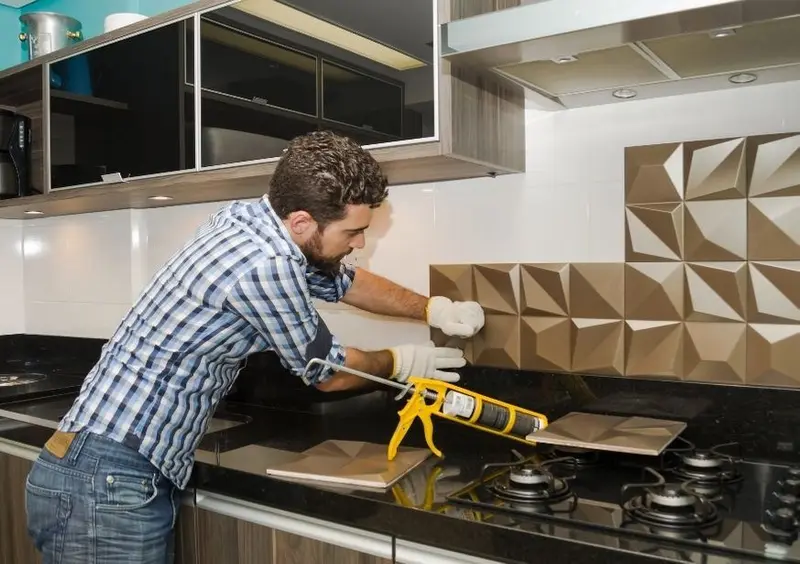 Man applying adhesive to fit a tiled kitchen splashback above a gas hob