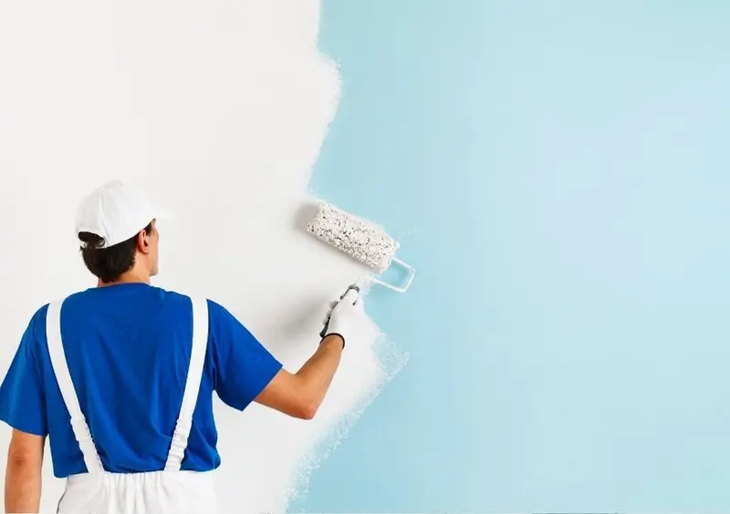 Painter rolling white paint over a light blue interior wall